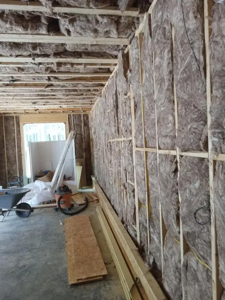 Interior of a building under construction, showing insulation in walls and ceiling. Wooden studs and beams are visible.