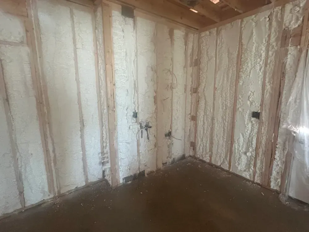 Interior view of a room with exposed wooden studs and walls insulated with white spray foam.