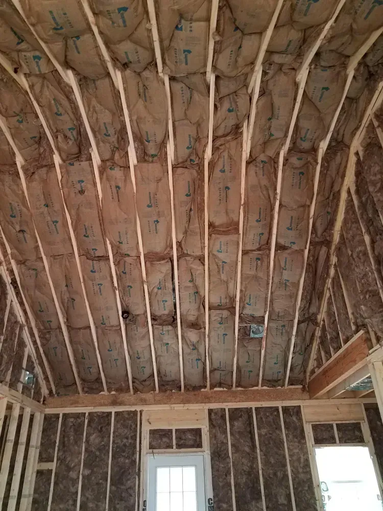 Interior view of a building under construction, showing wooden framing and insulation in the ceiling and walls.