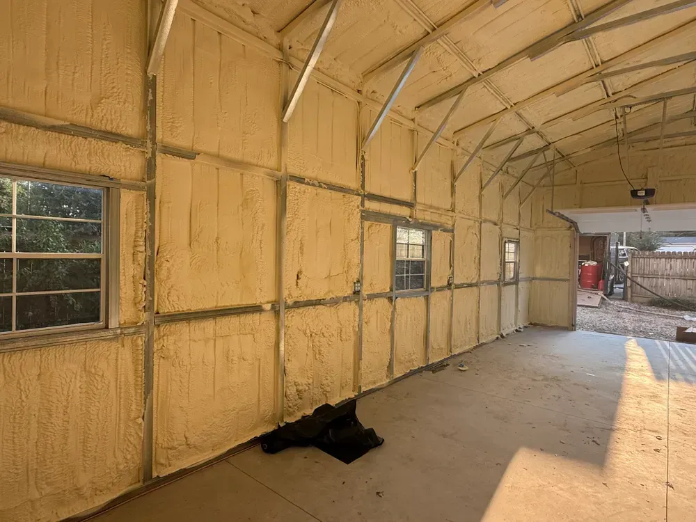 Interior of a building with spray foam insulation on the walls. Windows and a garage door are visible.