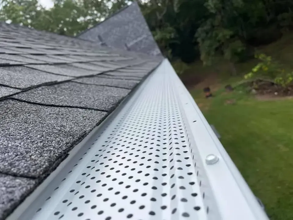 White gutter with perforated cover attached to a gray shingled roof, angled view.