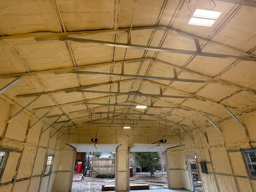 Interior view of a building's metal frame, insulated with yellow foam. Features open doorways and skylights.