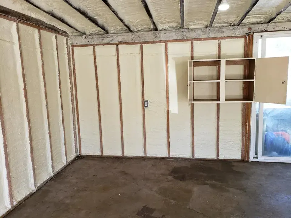 Interior of a room with spray foam insulation on walls and ceiling, unfinished concrete floor.