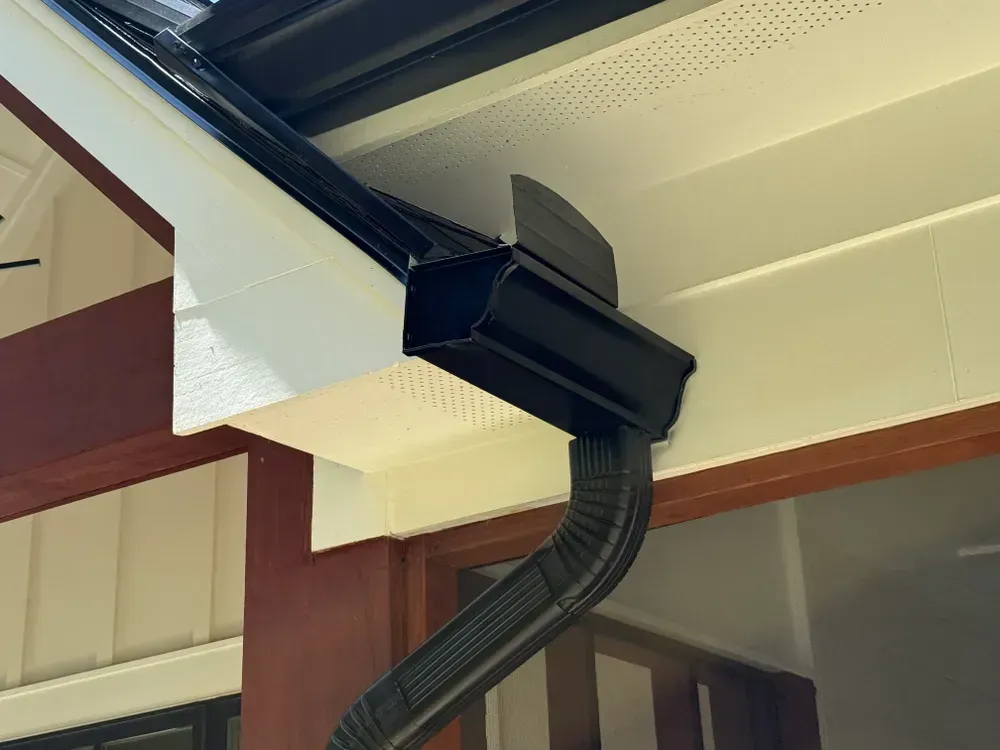 Black gutter and downspout on a white house exterior.