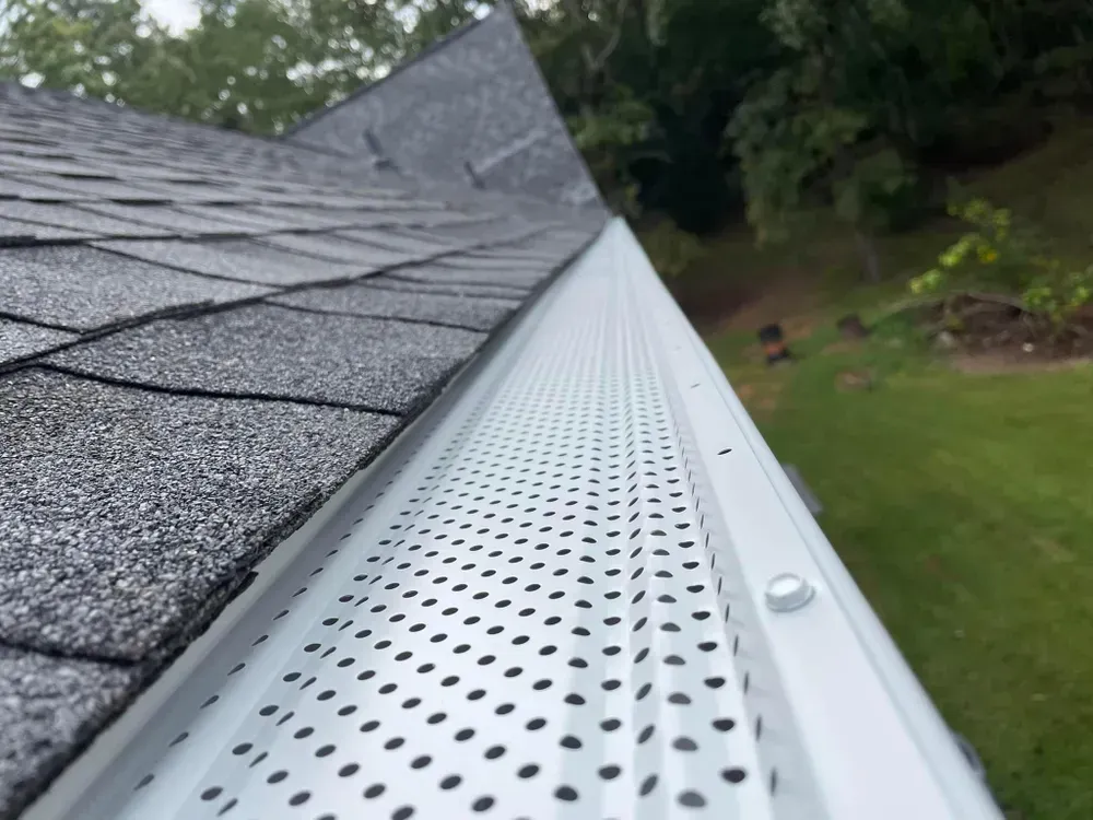 White gutter guard on a gray shingled roof, trees in the background.
