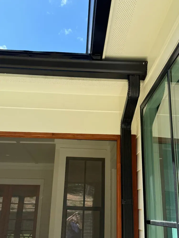 Black gutters installed on a light beige house under a bright blue sky.