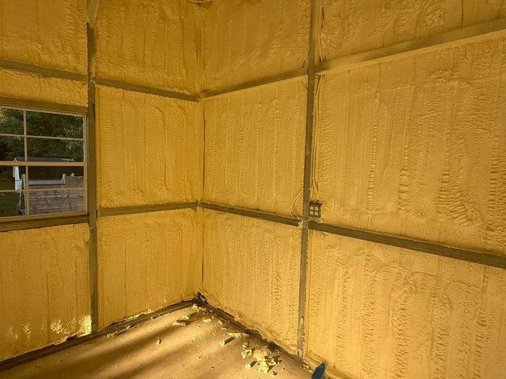Interior of a building with spray foam insulation covering walls and ceiling; window visible.