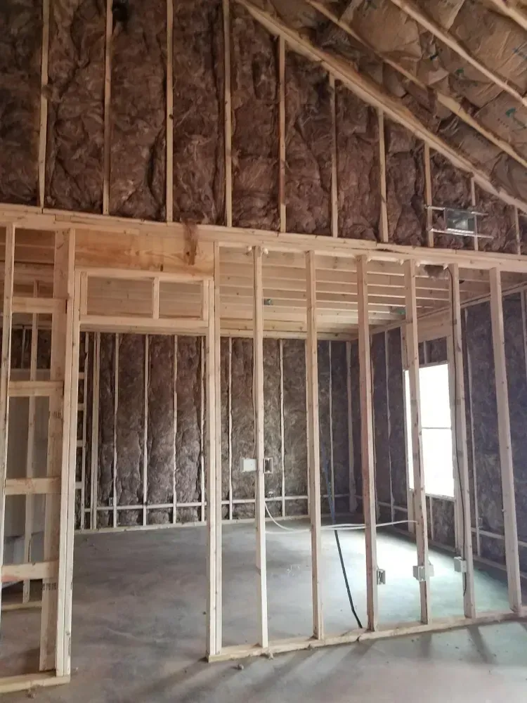 Interior view of a building under construction, showing wooden framing, insulation, and a concrete floor.