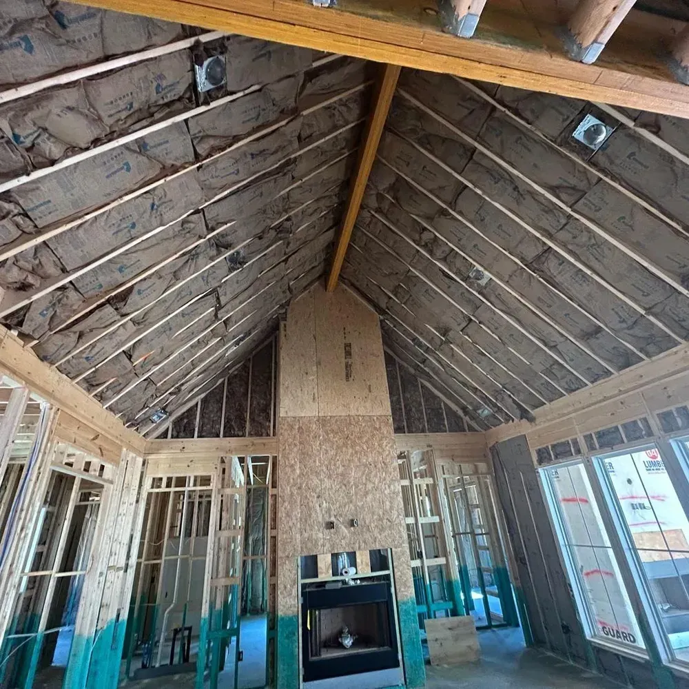 Interior framing of a house under construction with exposed beams, insulation, and a fireplace.