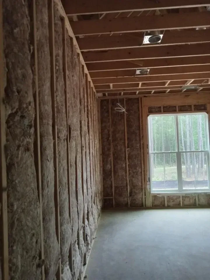 Interior of a building under construction, showing wooden studs, insulation, and a window with outside view.