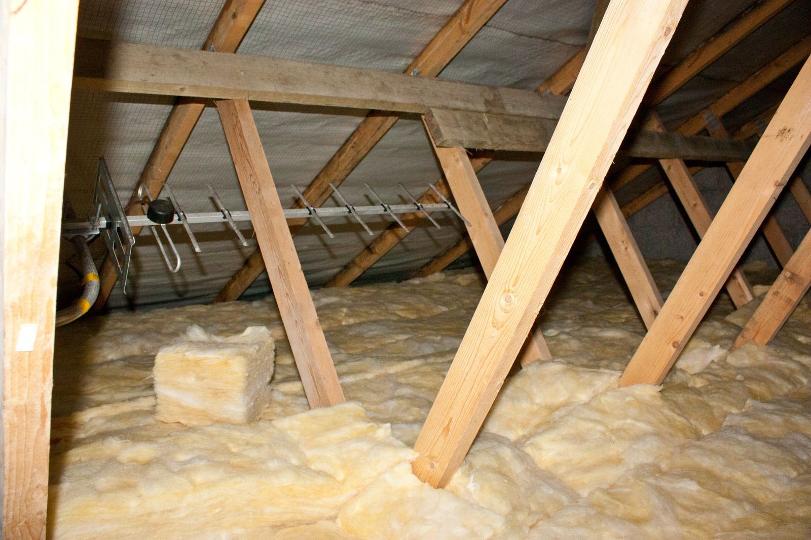 Interior view of an attic with insulation and wooden beams. A TV antenna is visible.