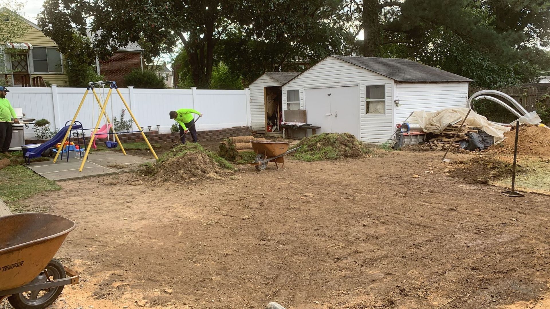 A yard with a wheelbarrow and a shed in the background.
