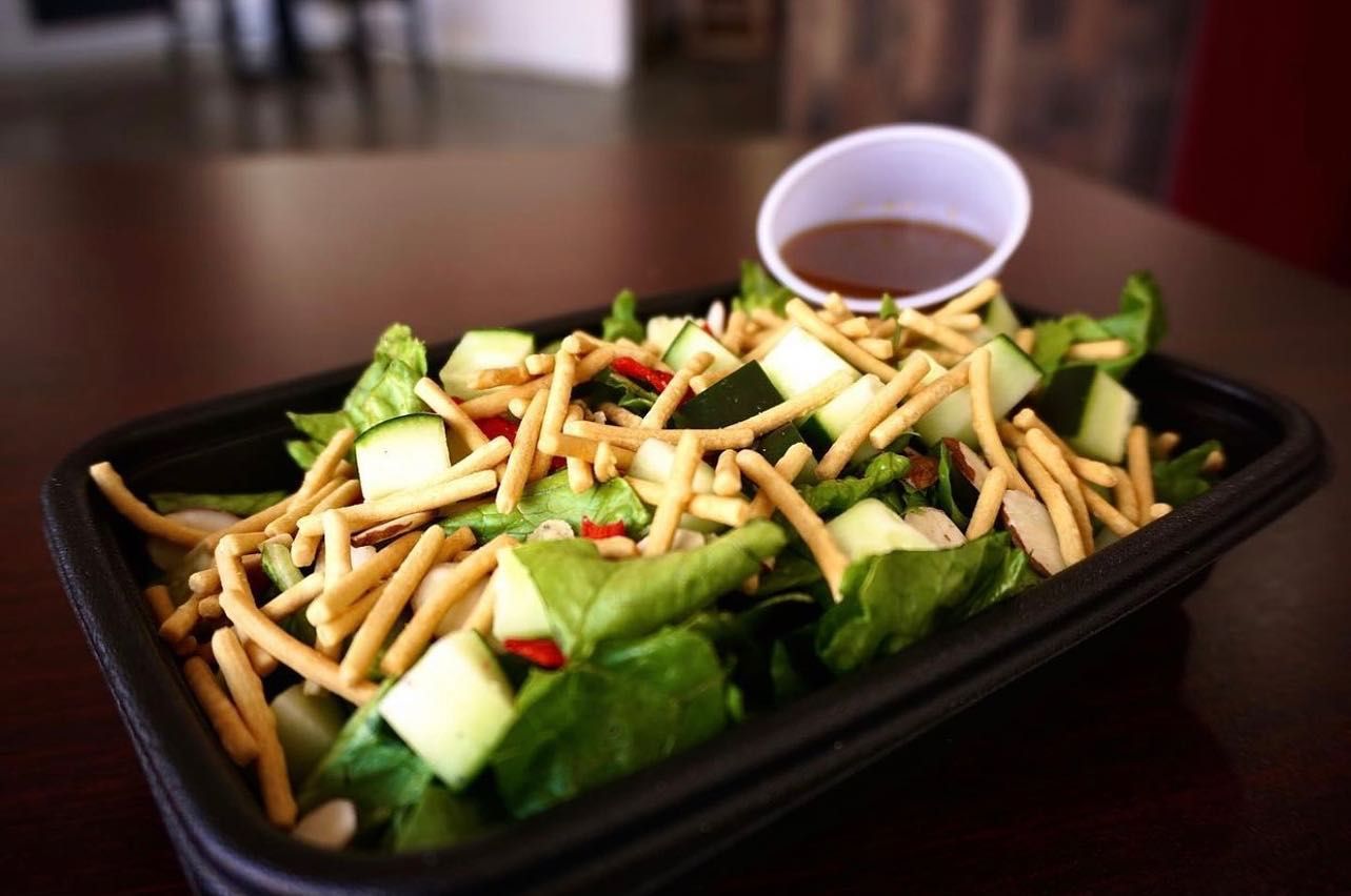 A salad with noodles and vegetables in a plastic container on a table.
