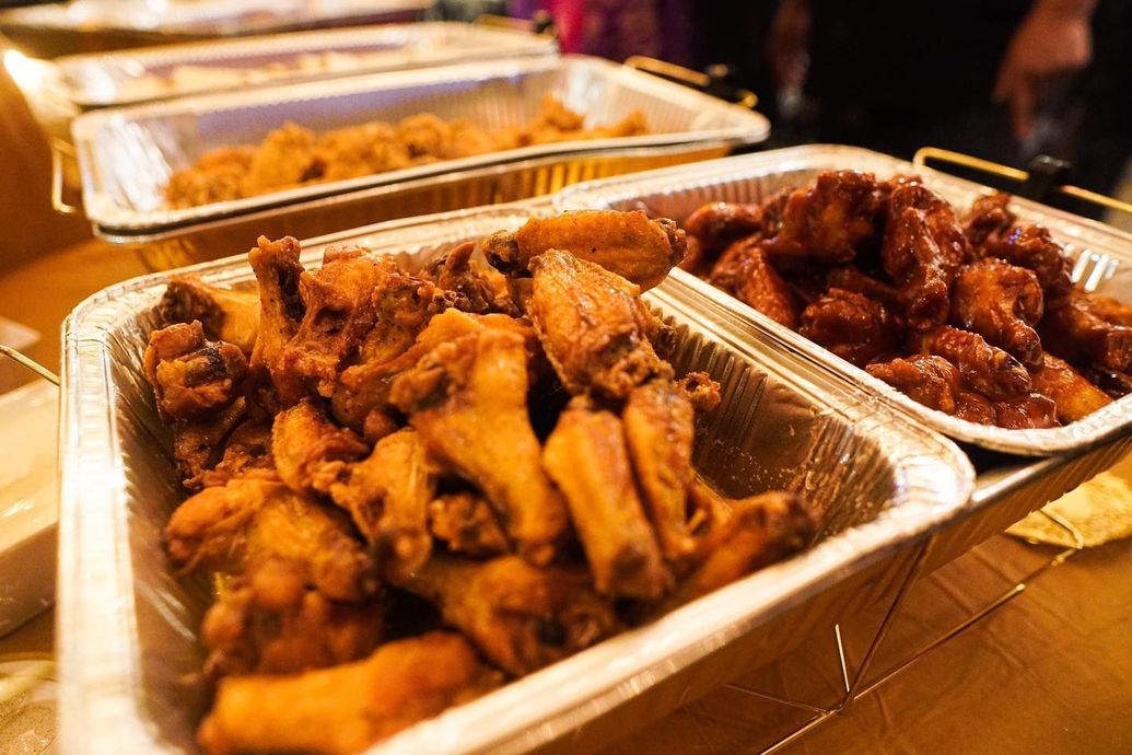 There are many trays of chicken wings on the table.