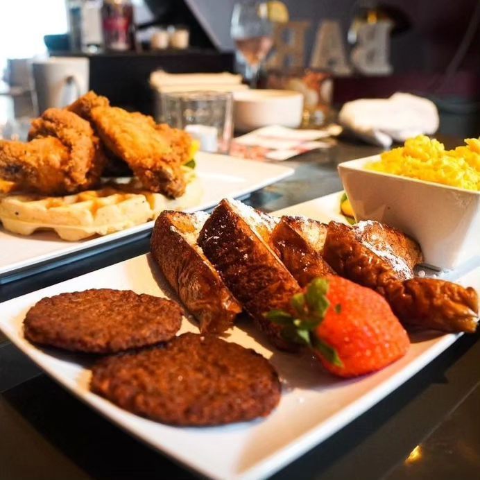 A plate of food on a table with a bowl of scrambled eggs in the background
