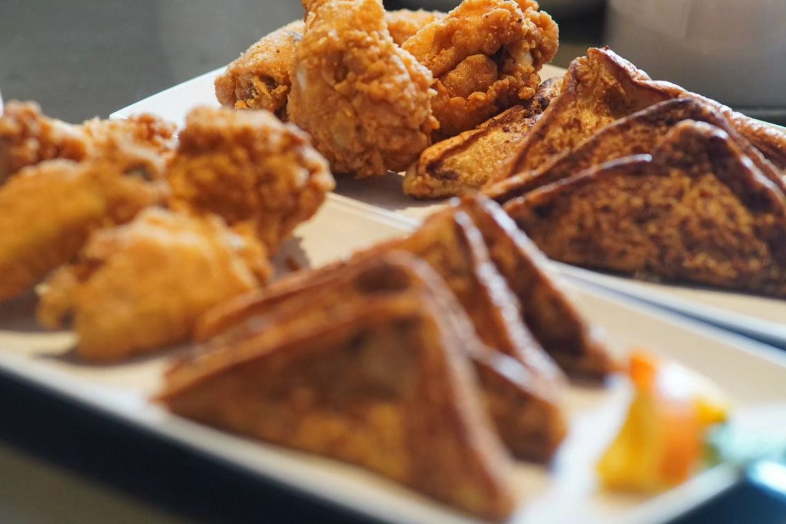 A white plate topped with fried chicken , french toast , and egg rolls.