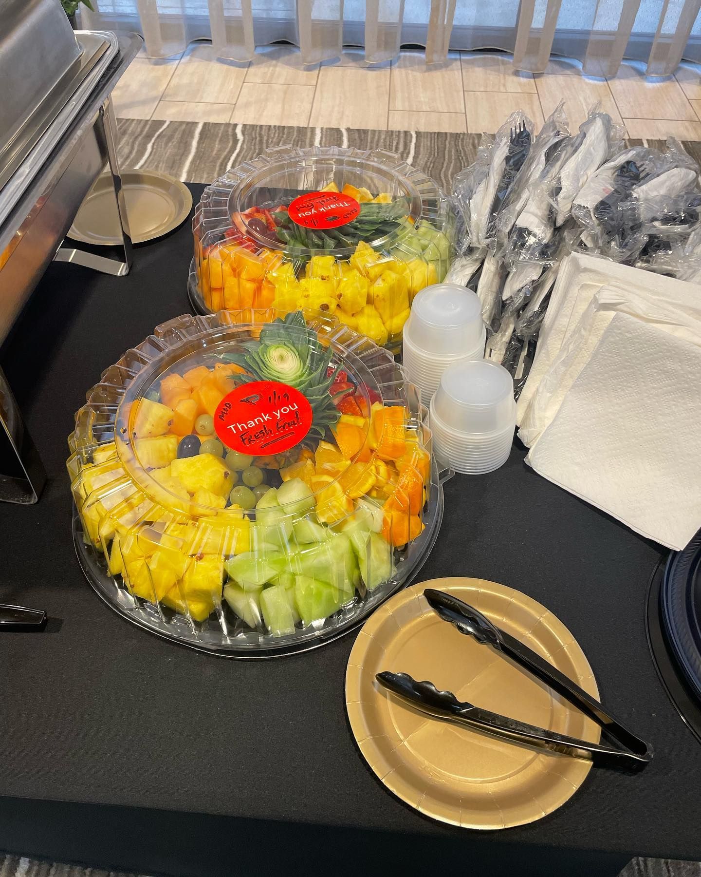A table with plates and tongs and a tray of fruit on it.