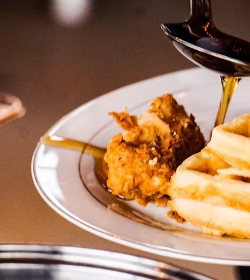 Syrup is being poured on a plate of fried chicken and waffles