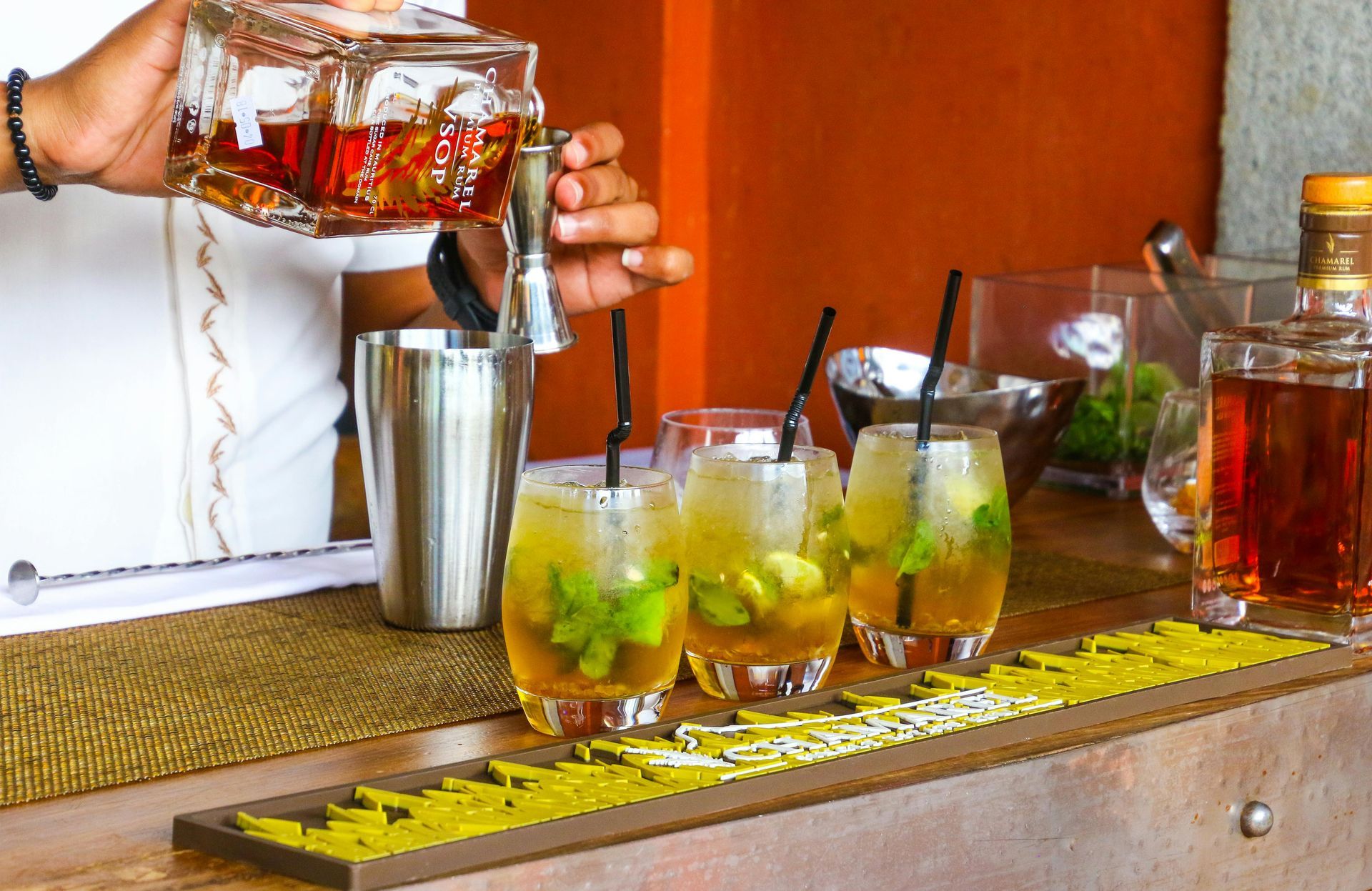 A bartender is pouring a drink into a glass with a straw.