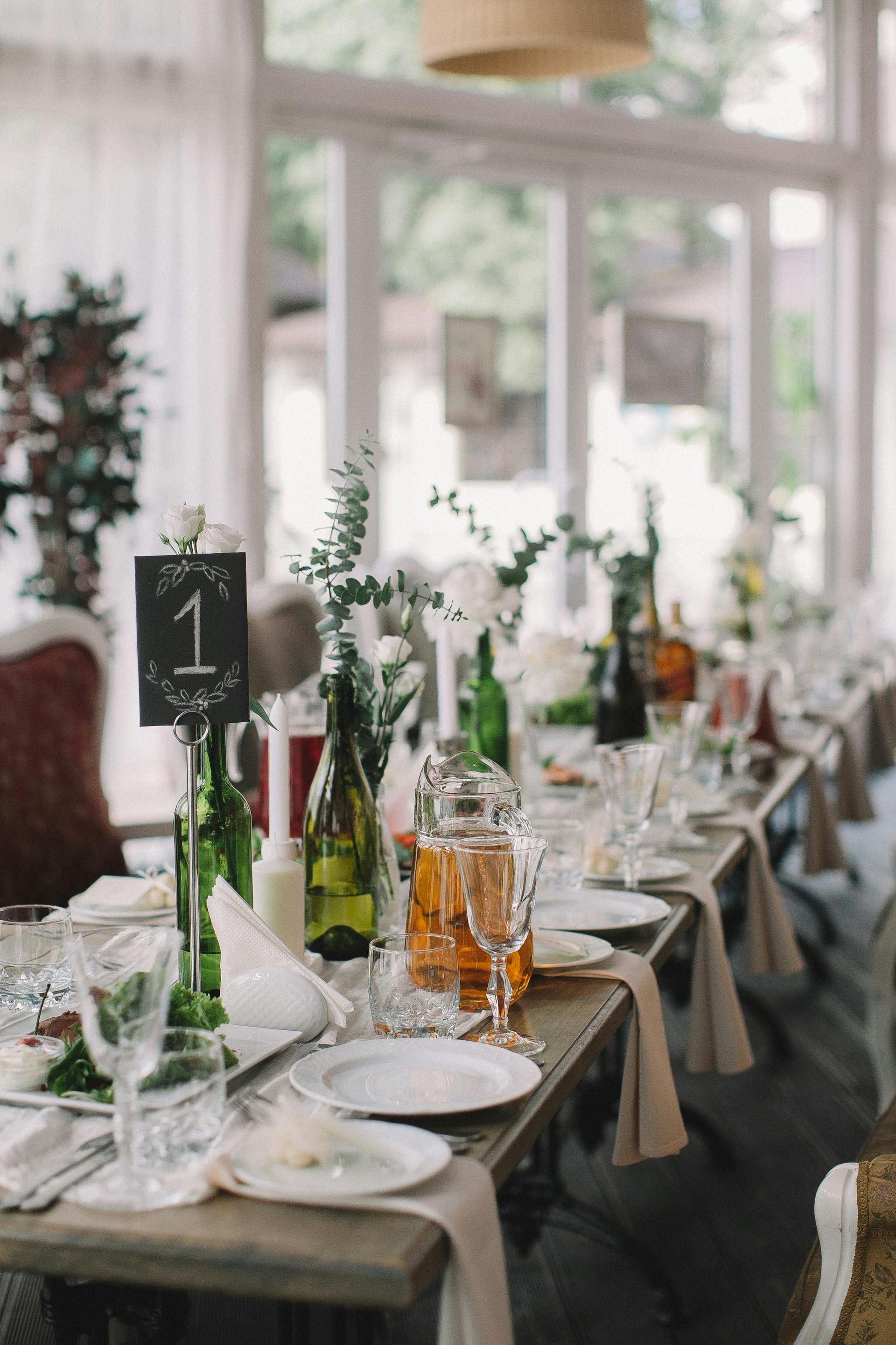 A long table set for a wedding reception with plates , glasses , and bottles.
