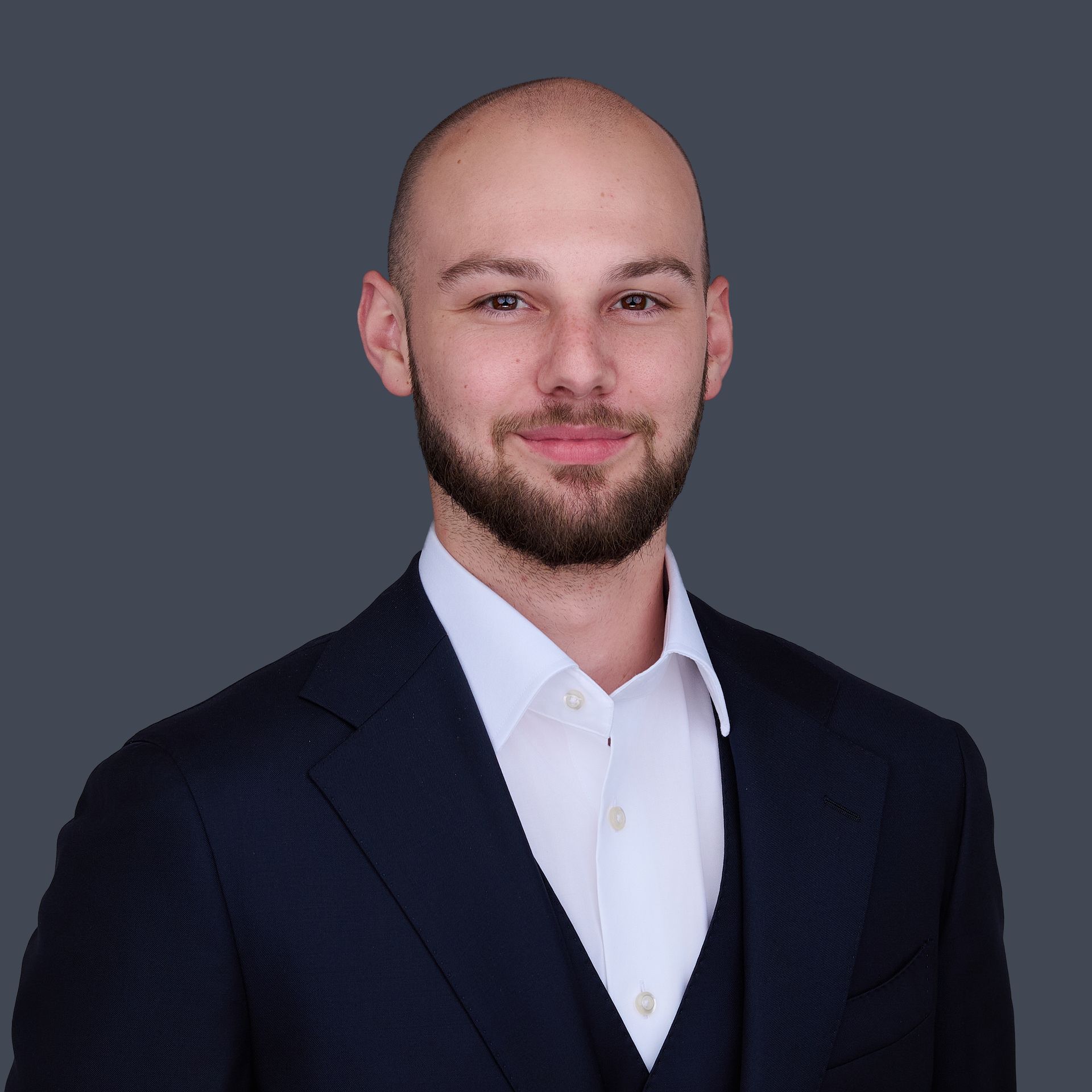 A bald man with a beard is wearing a suit and white shirt.