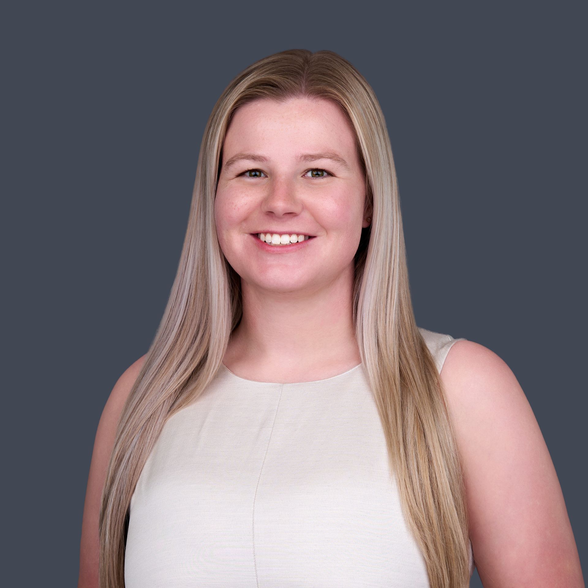 A woman with long blonde hair is wearing a white tank top and smiling.