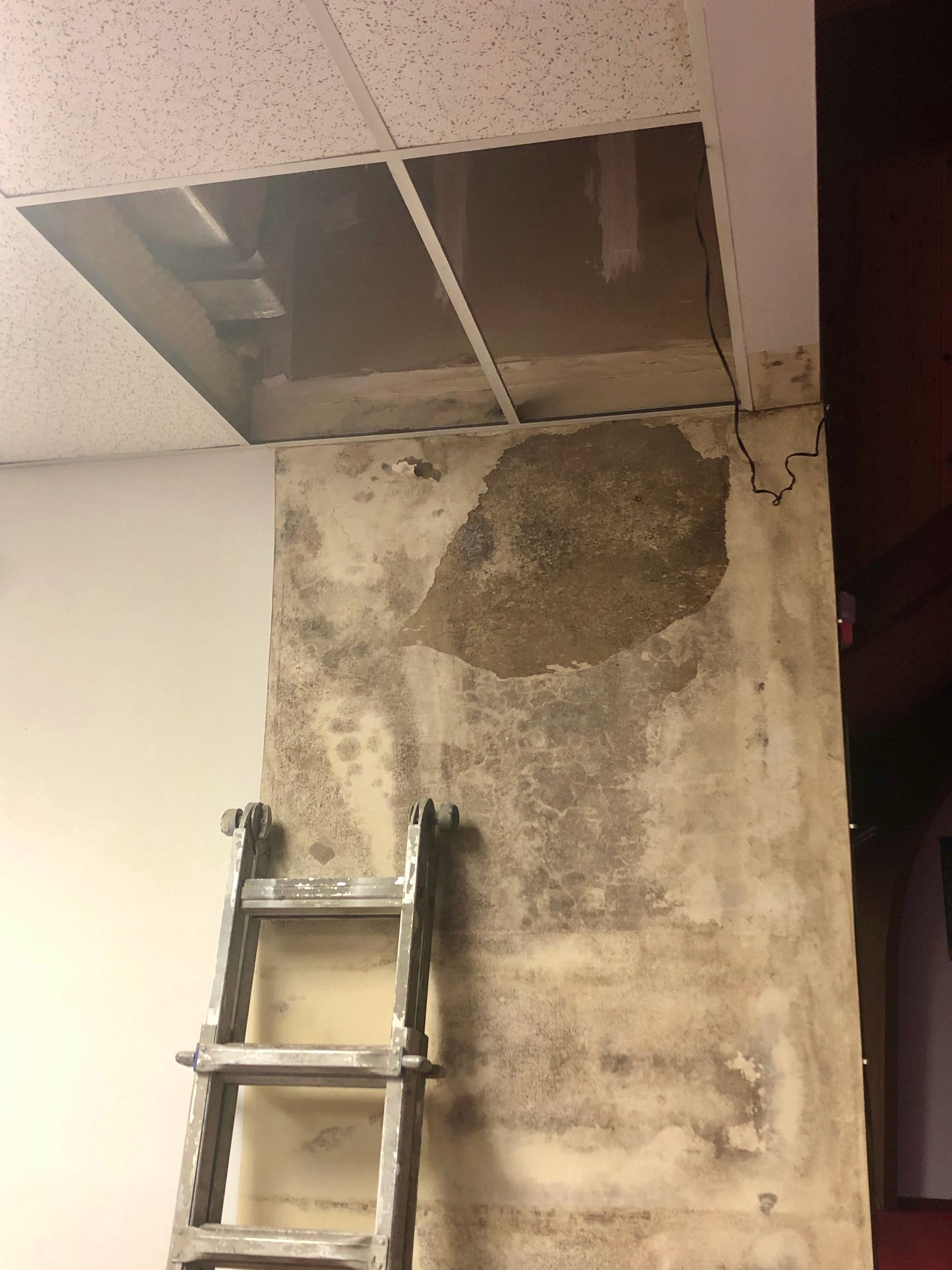 A ladder is leaning against a wall next to a hole in the ceiling.