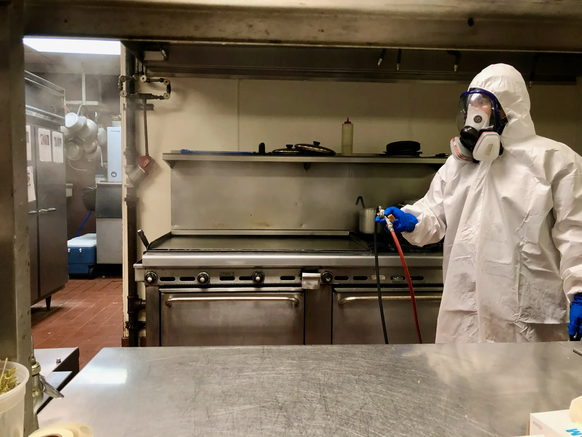 Person in hazmat suit spraying disinfectant in a commercial kitchen.