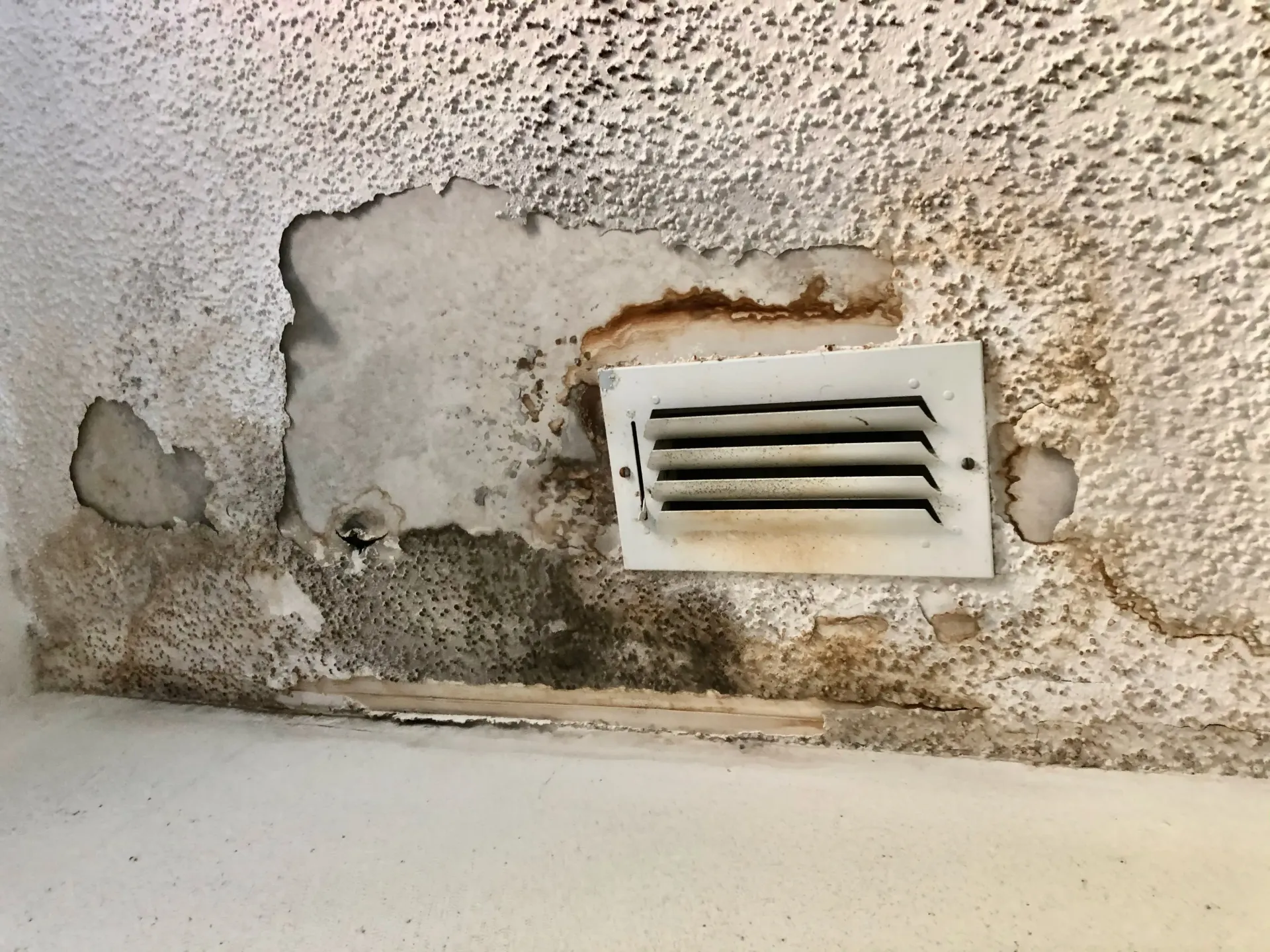 A white vent on a wall with peeling paint.