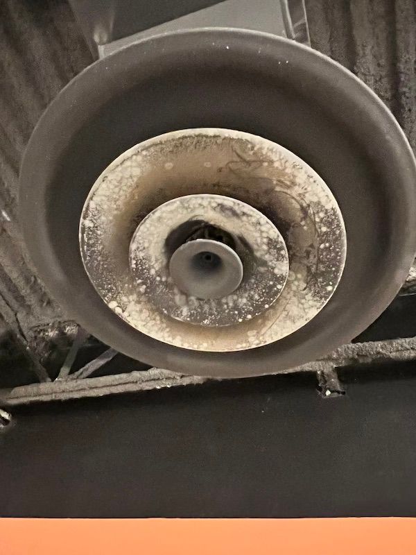 Dirty ceiling air vent with concentric circular grilles. White dust and grime covers the surface.