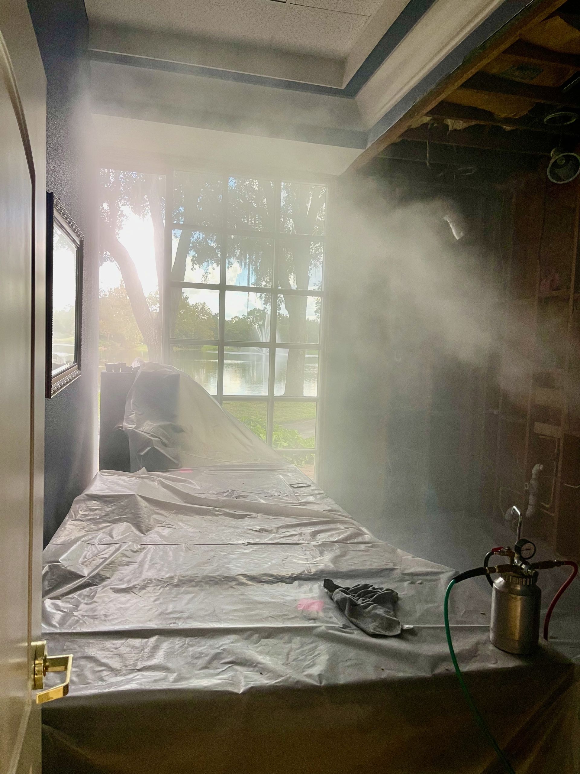 A room with a bed and a window with smoke coming out of it.