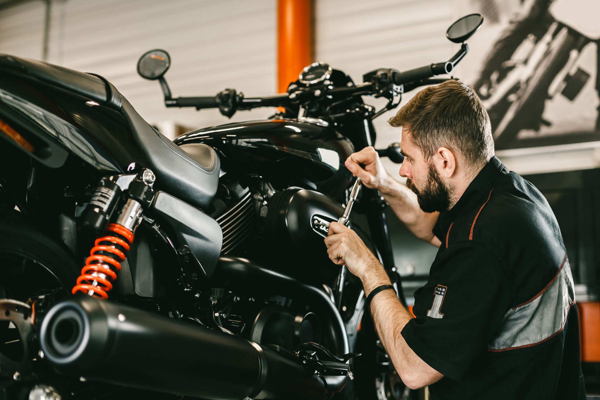 A mechanic in a back uniform performs motorcycle maintenance at a repair shop.