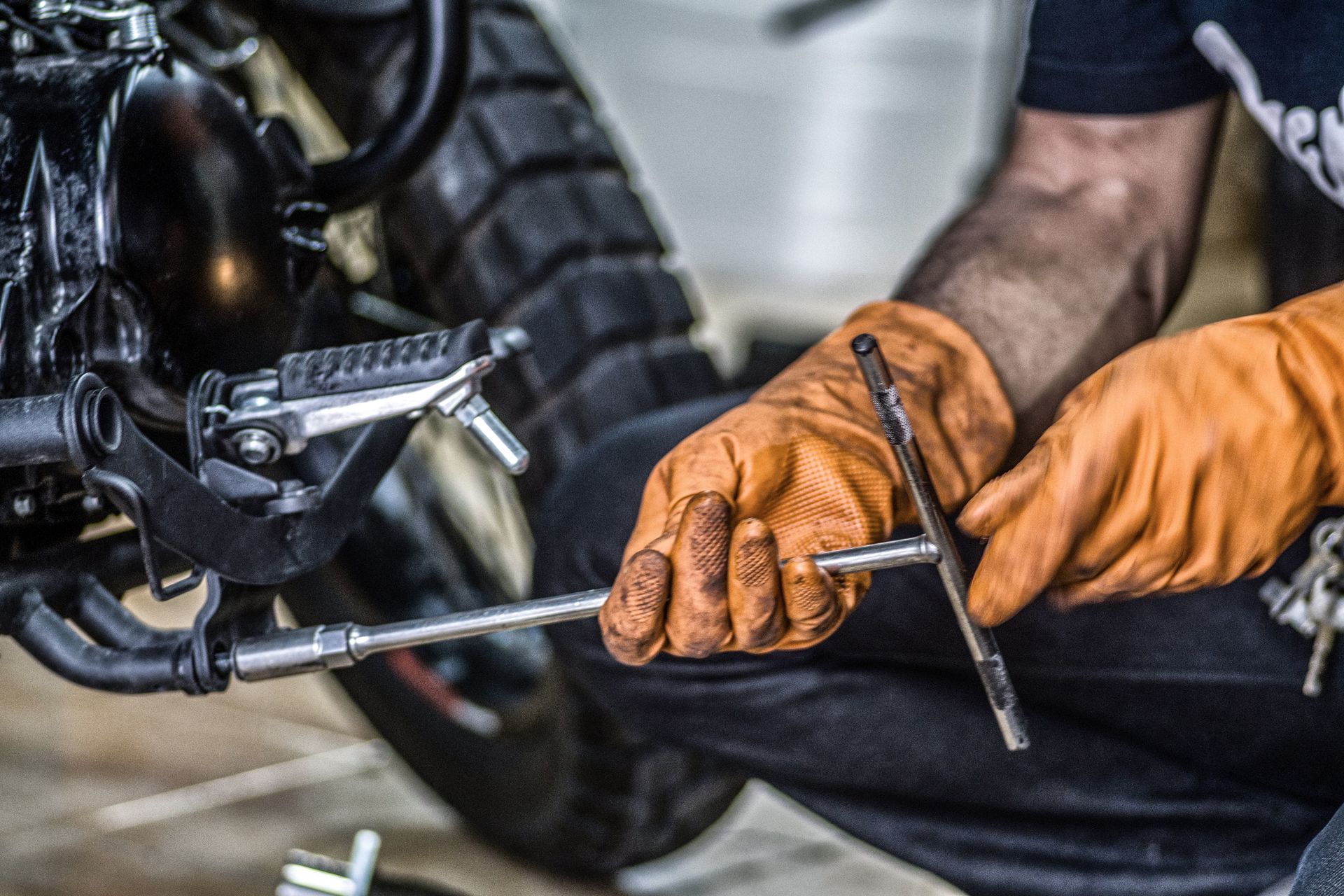 Motorcycle repair—mechanic in orange gloves working on a motorcycle engine.