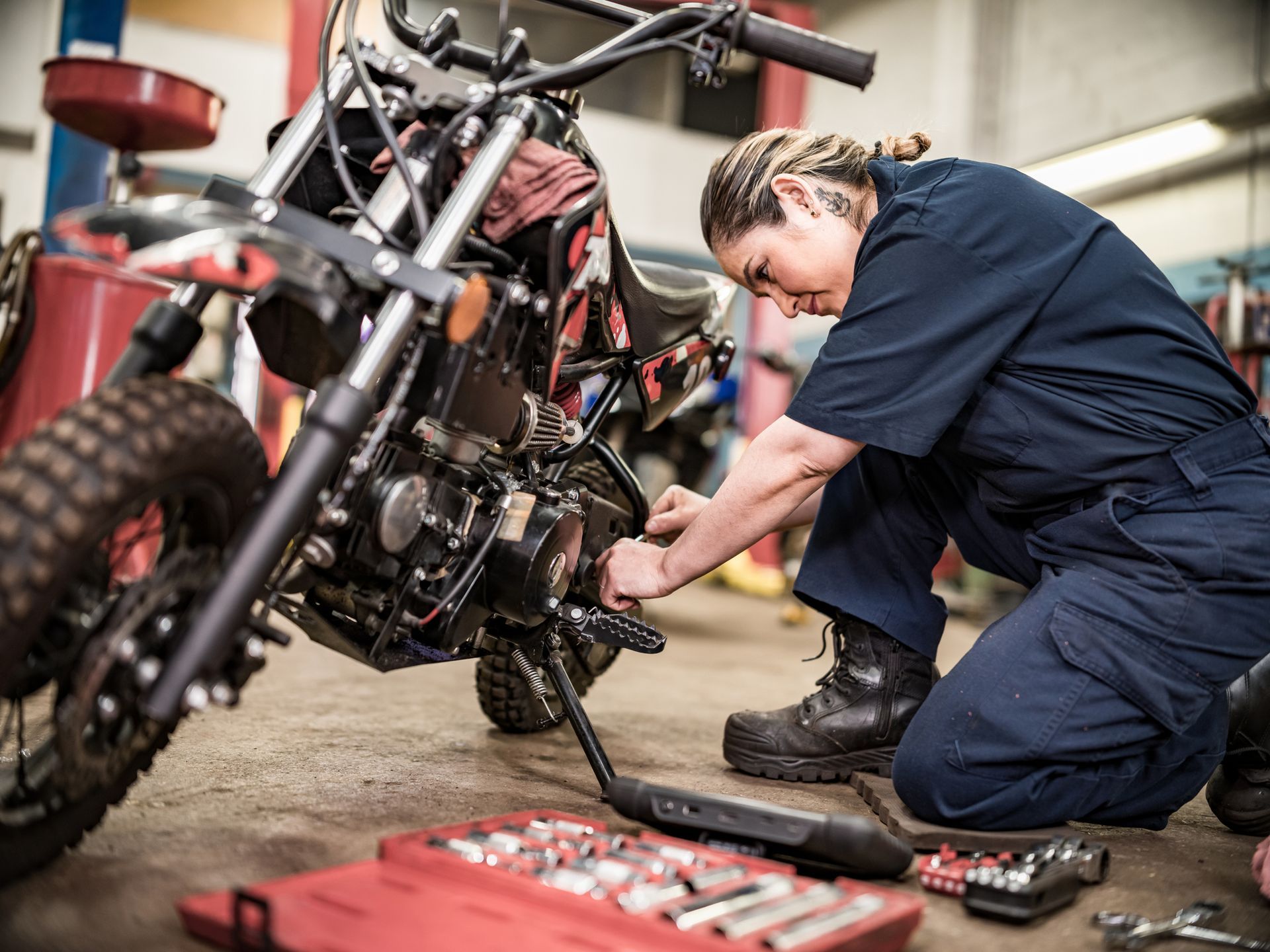 A woman working on motorcycle repair in a garage, demonstrating hands-on skills with tools nearby.