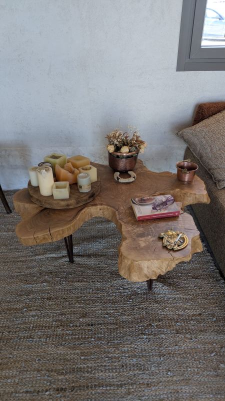 Tavolino da caffè in legno con bordo naturale, candele, fiori e libri, vicino a un divano.