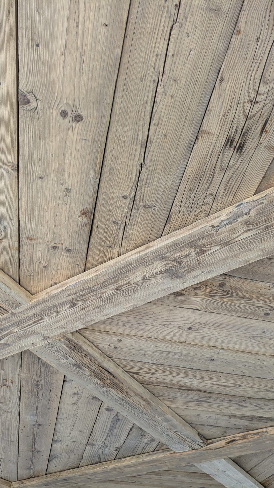 Soffitto in legno con travi e assi, invecchiato, nei toni del grigio e del marrone.