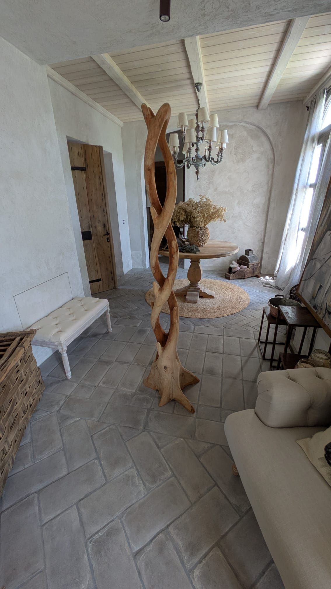 Scultura in legno in una stanza piena di luce con divano bianco, panca e pavimento di colore neutro.