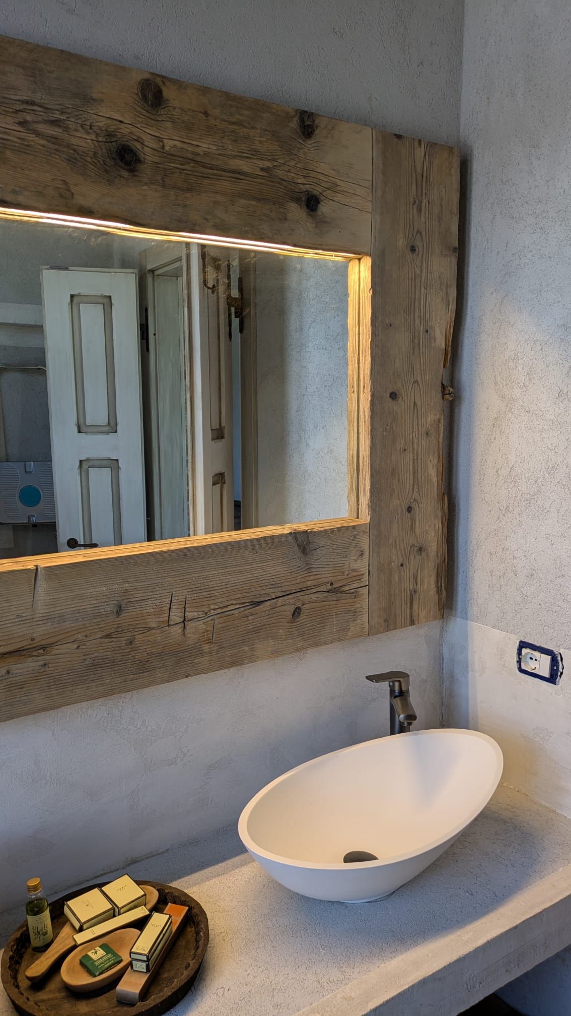 Bagno con specchio rustico con cornice in legno, lavabo a appoggio e articoli da toeletta su un vassoio.