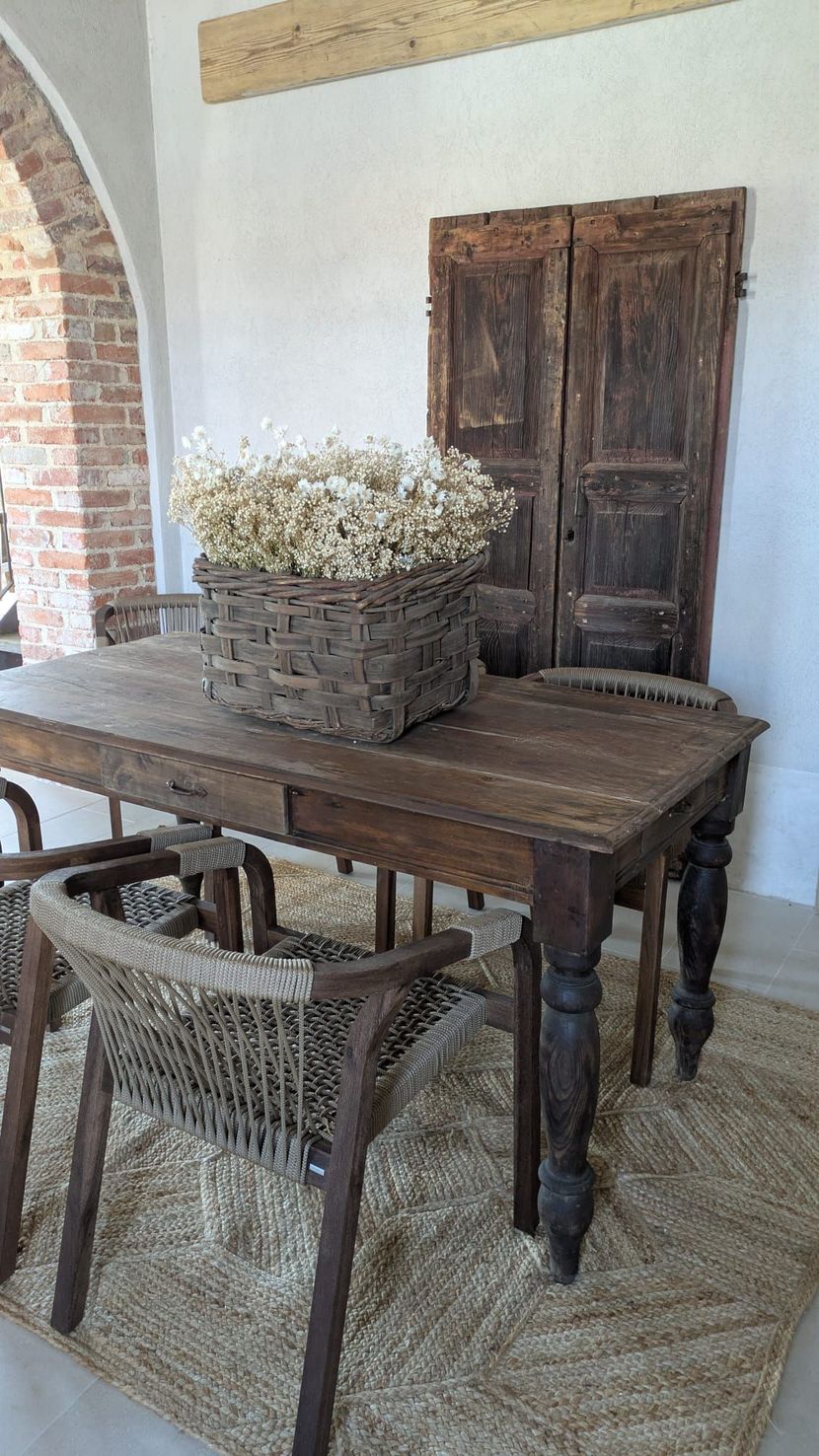 Tavolo e sedie in legno con un cesto di fiori secchi; interno rustico.