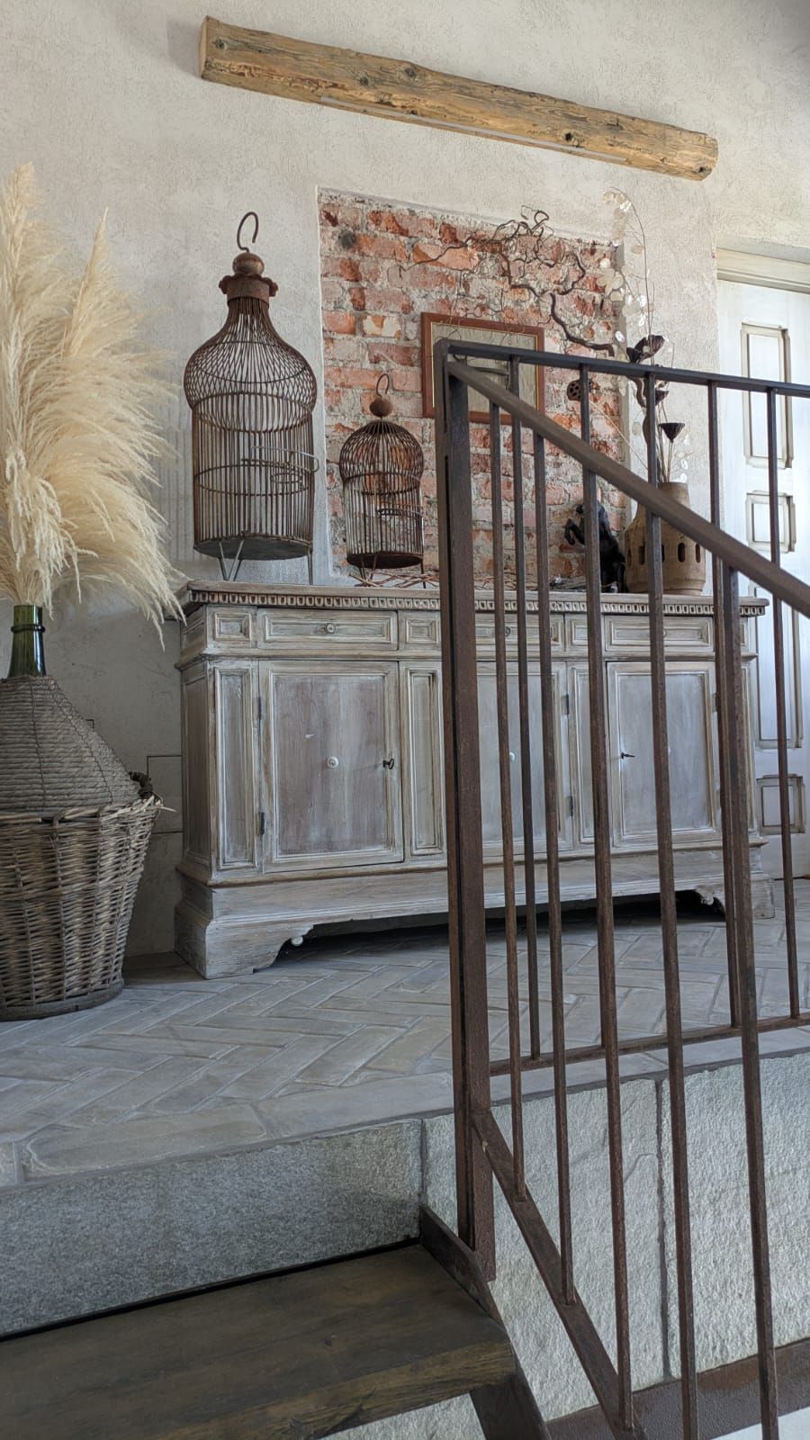 Mobiletto rustico in legno con gabbie per uccelli e decorazioni, contro un muro di mattoni, vicino a una scala.