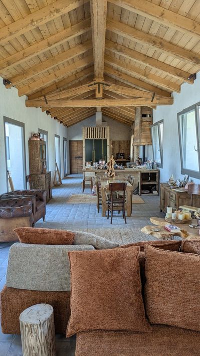 Ampia zona giorno rustica con soffitto con travi in ​​legno, cucina a vista e sedute marroni/beige.