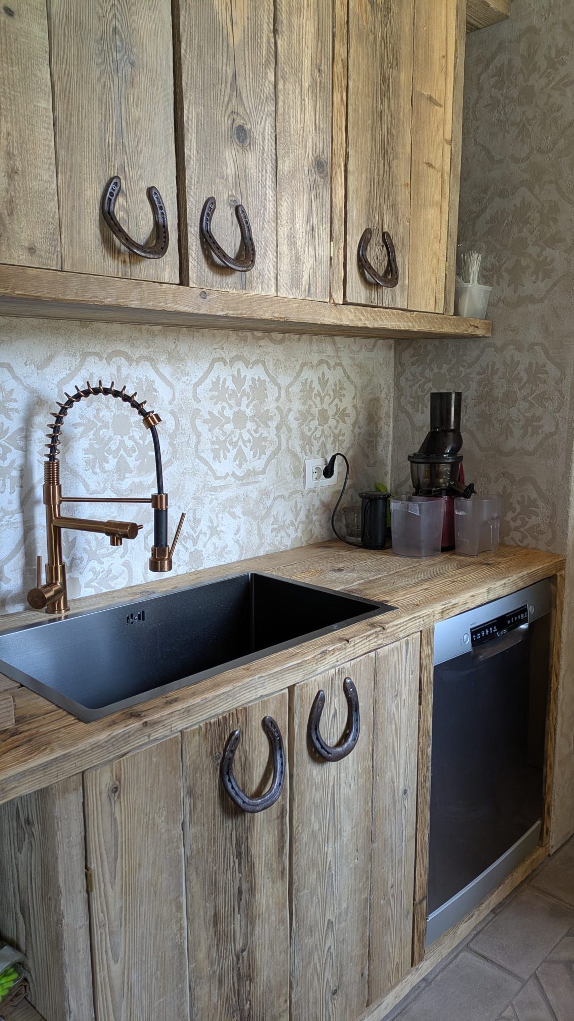 Cucina rustica con mobili in legno, maniglie a ferro di cavallo, lavello nero e rubinetto in rame.