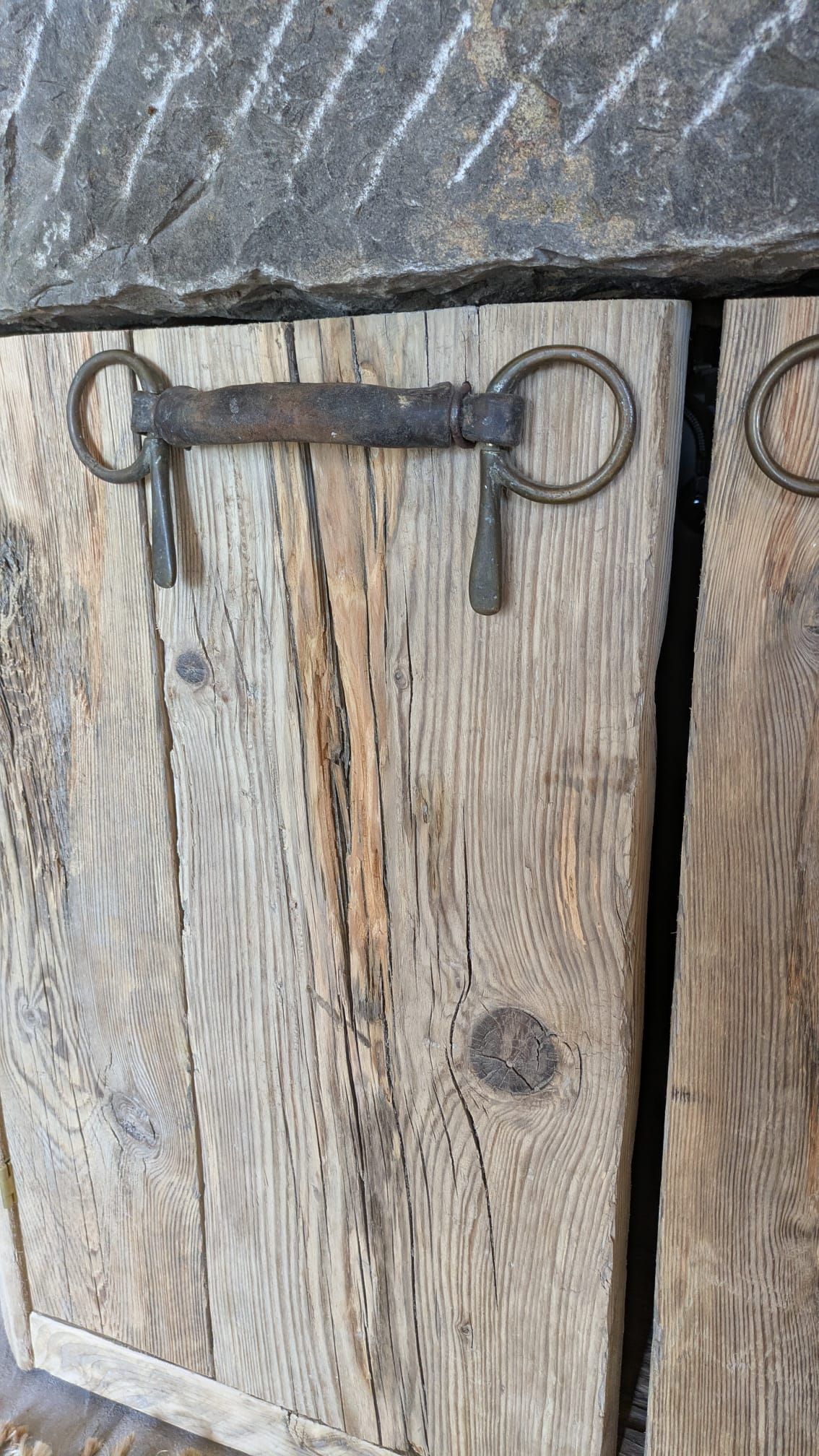 Primo piano di porte in legno invecchiato con maniglia e cerniere in metallo, appoggiate a un muro in pietra ruvida.