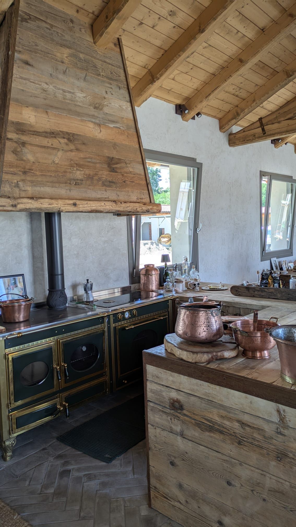 Cucina rustica con stufa e cappa rivestite in legno, pentole in rame e dettagli in legno.