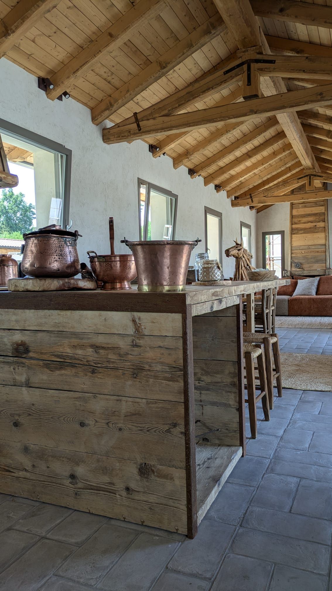 Cucina rustica con isola in legno, pentole in rame e soffitto con travi a vista.