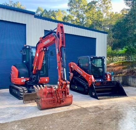 A Flatbed Truck next to an Orange Kubota Excavator — Wal's Concreting Service in North Casino, NSW