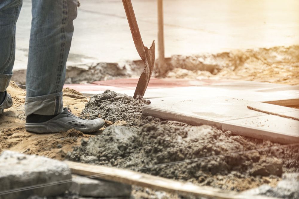 Person in Jeans Digging in Dirt with A Pickaxe at A Construction Site — Wal's Concreting Service in Lismore, NSW