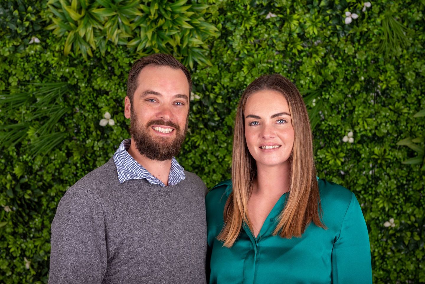 Man and woman smiling in front of a green plant wall — Remote Assistant In Braitling, NT