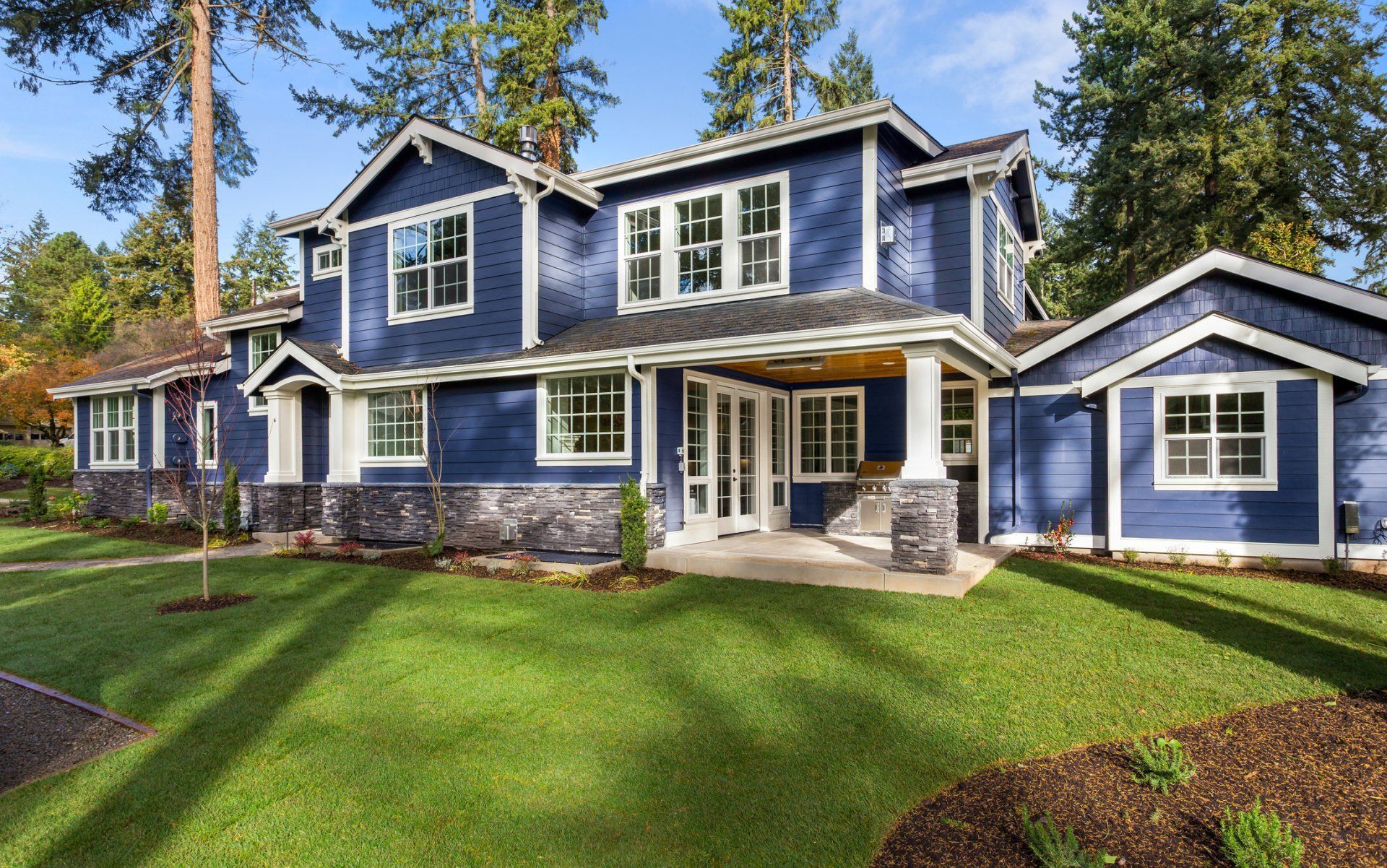 A large blue house with a lot of windows is sitting on top of a lush green lawn.