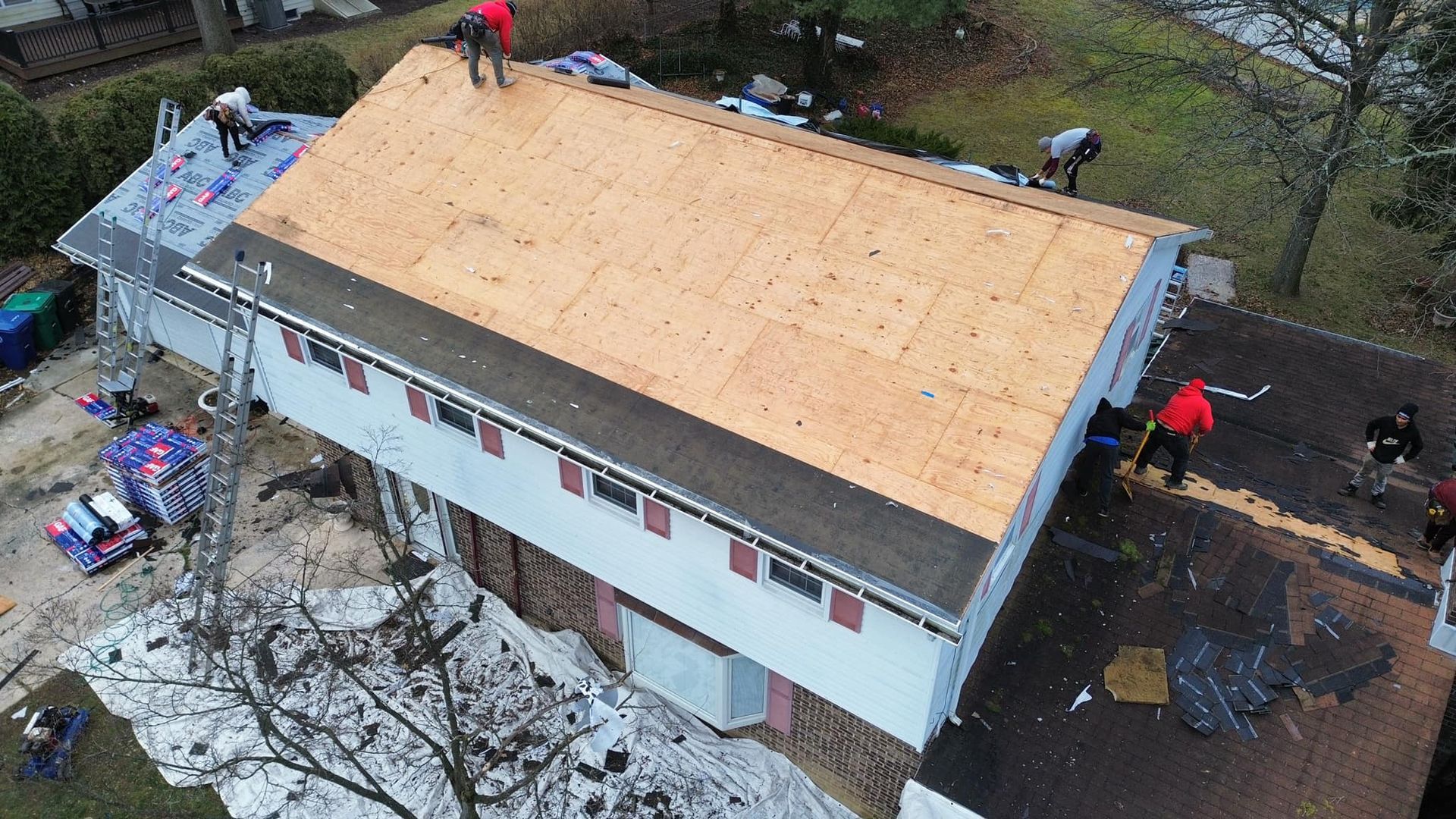 Aerial view of workers replacing a residential roof, installing new plywood sheeting over the roof frame.